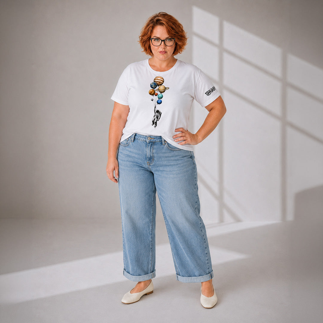 Woman wearing a white t-shirt with graphic designs and blue jeans in a well-lit room.