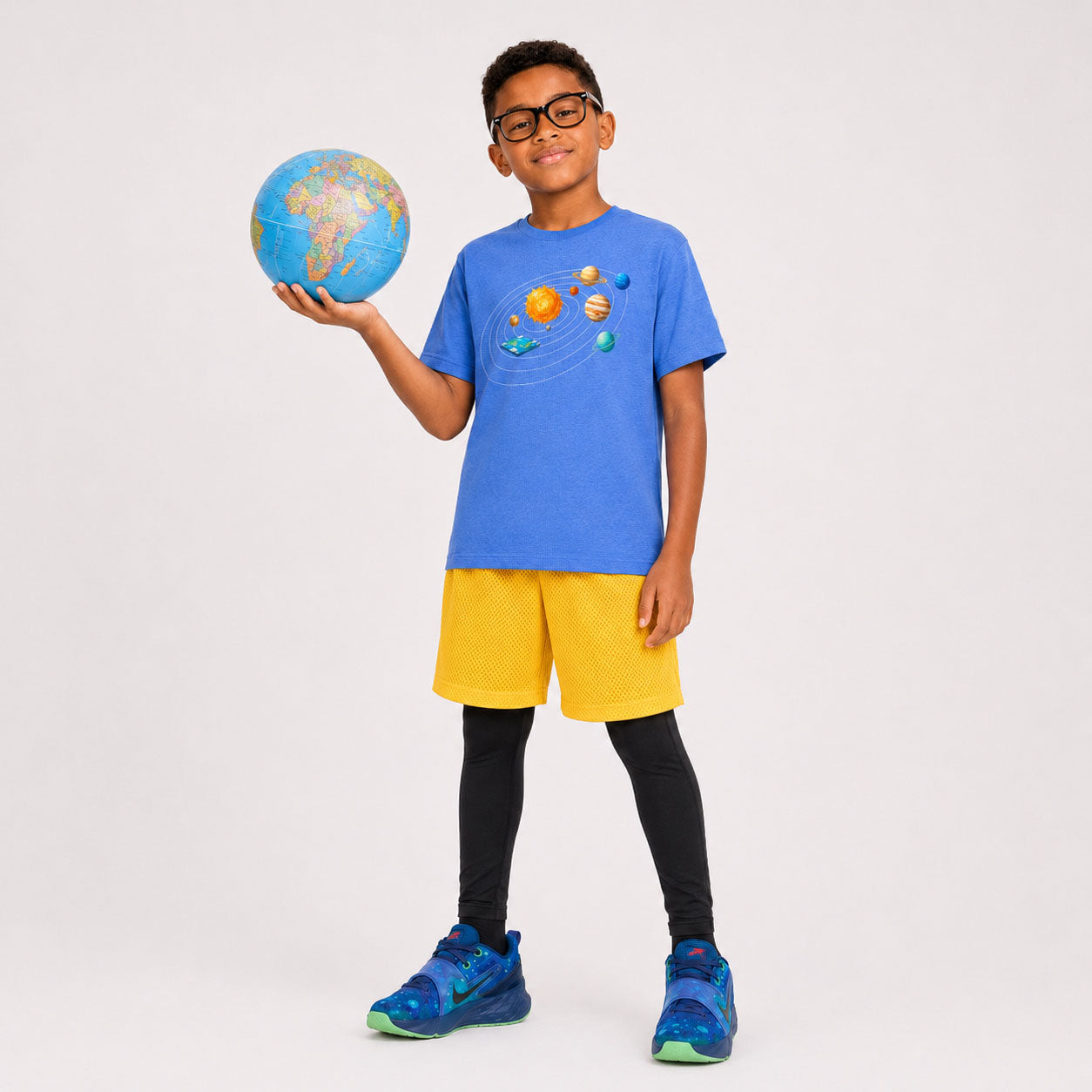 Child holding a small globe wearing a blue t-shirt with solar system design on a plain background